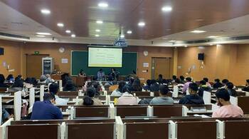 Five panelists sit on a stage discussing "Drawn to Discovery! SciComm Exhibition & Panel Discussion" displayed on a screen. A large audience of students is seated in rows in the lecture hall, facing the stage.