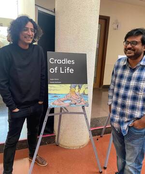 Two smiling men stand beside a black poster titled "Cradles of Life" by Argha Manna and Saurja DasGupta, which features an illustration of volcanic islands.